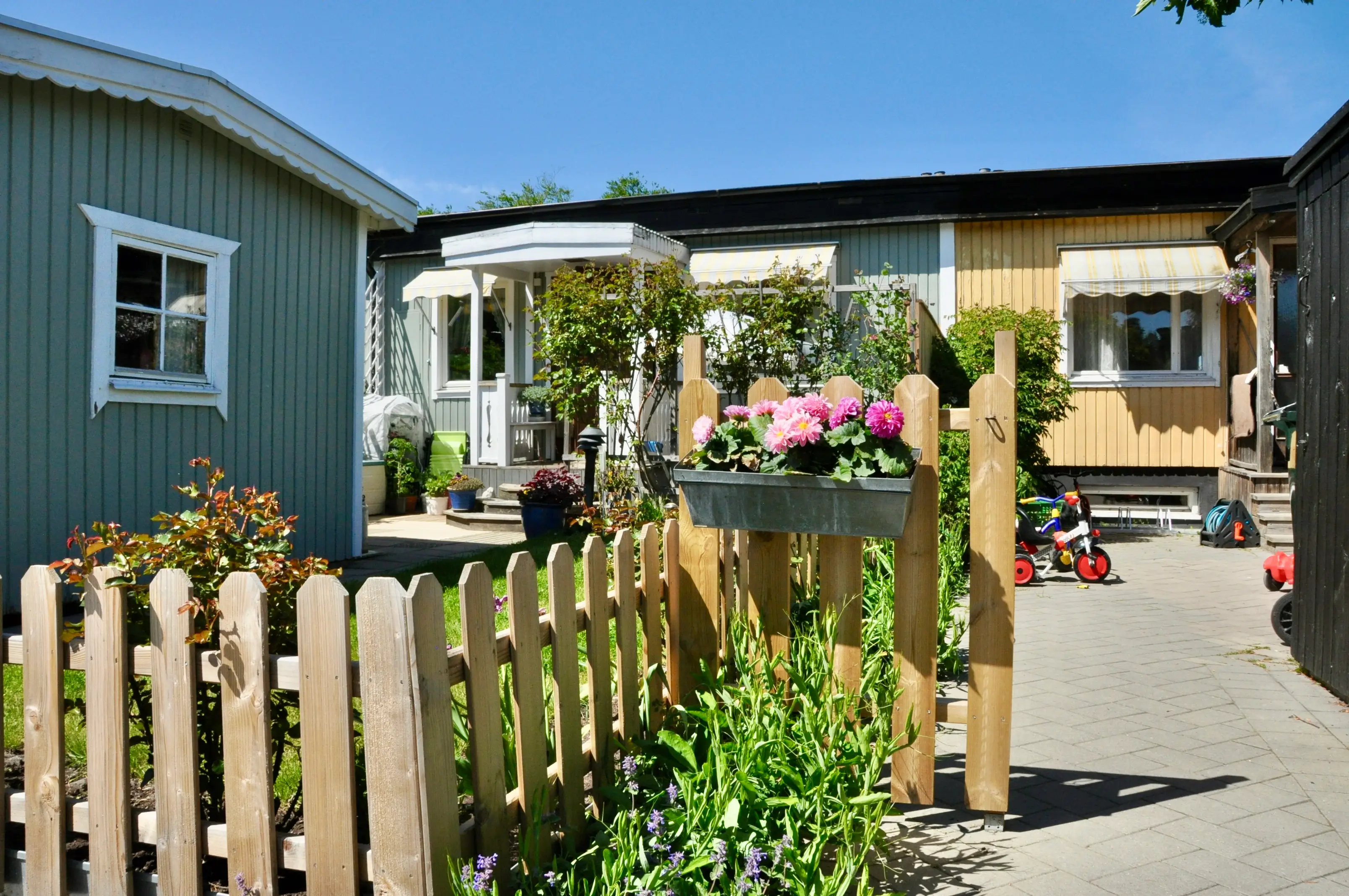 Trädgård med grind och blomlåda framför ett av husen.