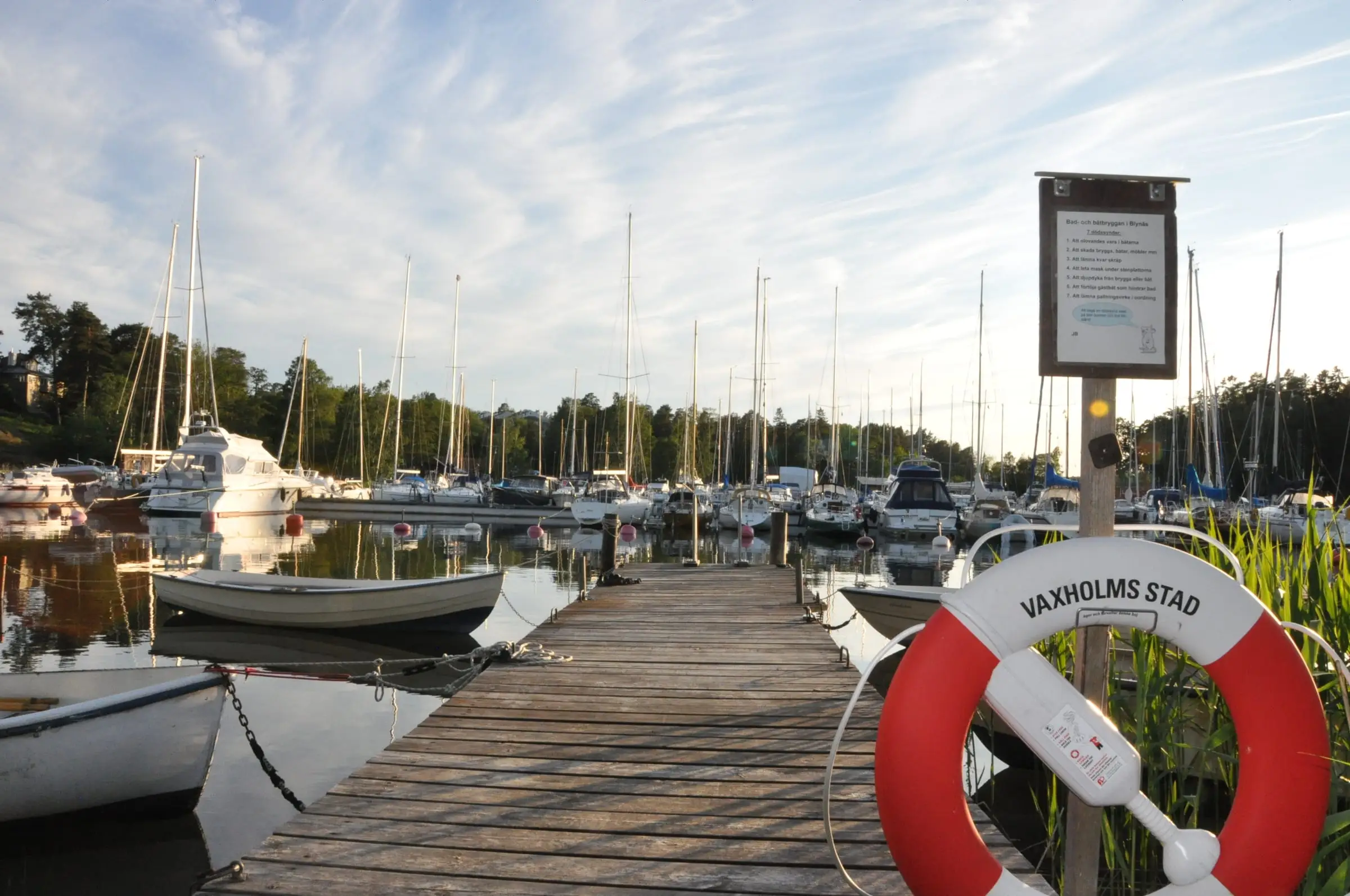 Träbrygga nedanför Blynäs med förtöjda båtar och en livboj märkt Vaxholms stad.